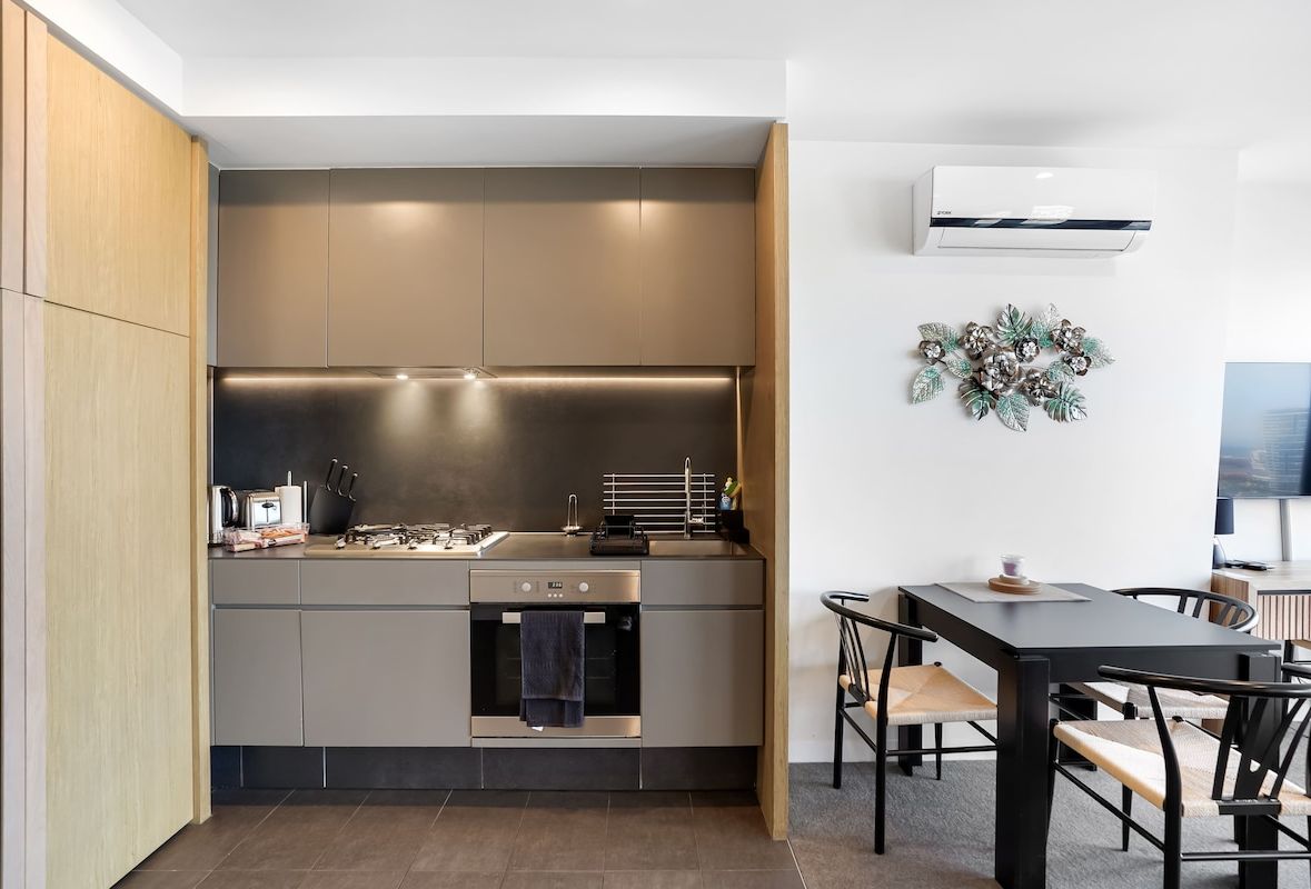 A modern kitchen with built-in appliances, a dining area with a table and chairs, and a wall-mounted air conditioner.