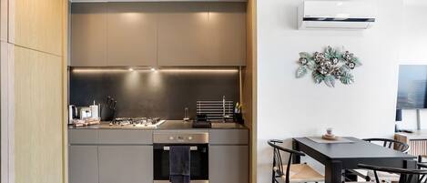 A modern kitchen with built-in appliances, a dining area with a table and chairs, and a wall-mounted air conditioner.