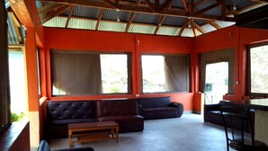 Una habitación con techo alto, paredes anaranjadas, un sofá negro, una mesa de madera y una zona de bar.