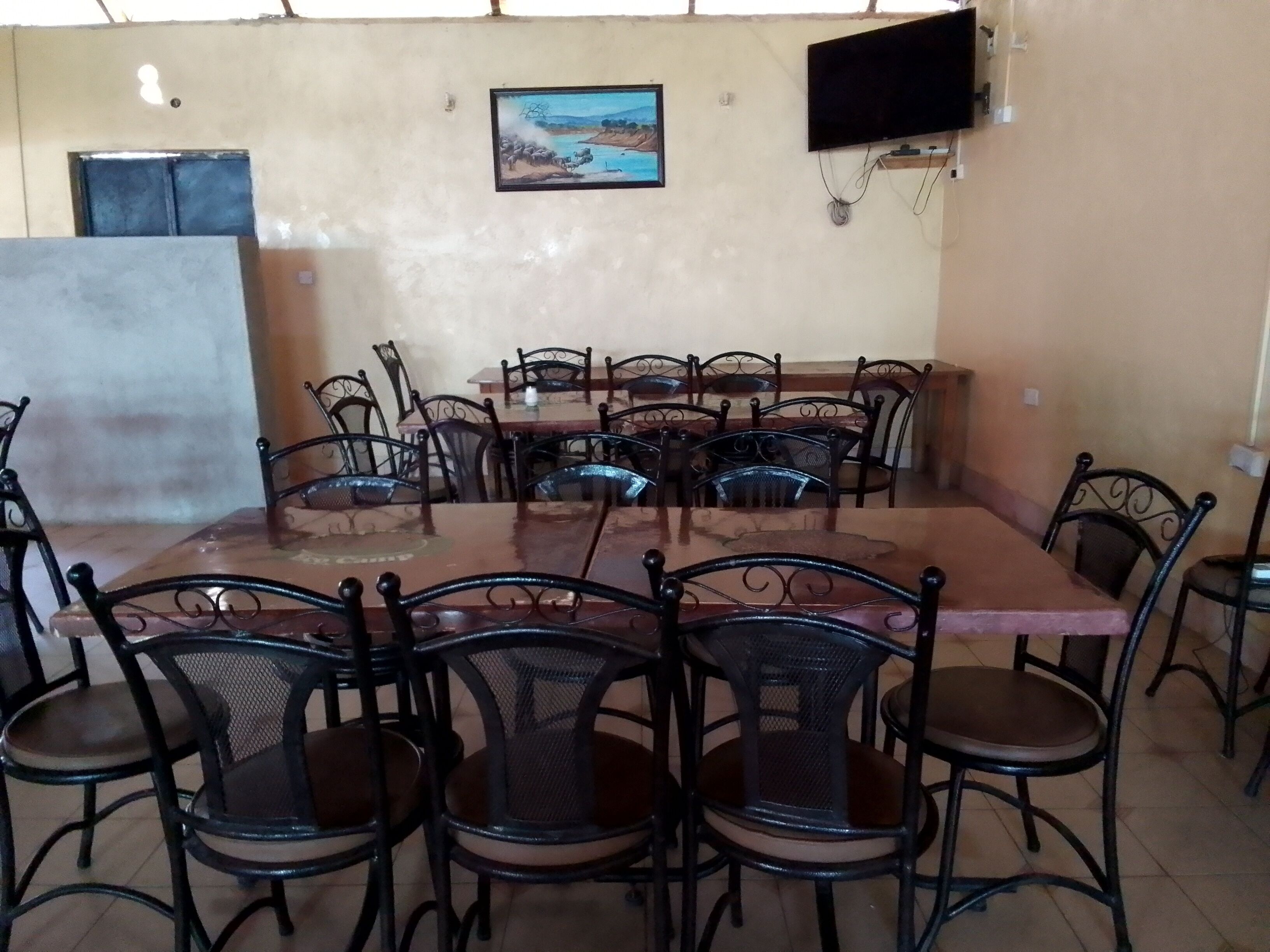 A dining area with a large wooden table surrounded by metal chairs, a television mounted on the wall, and a painting above the table.