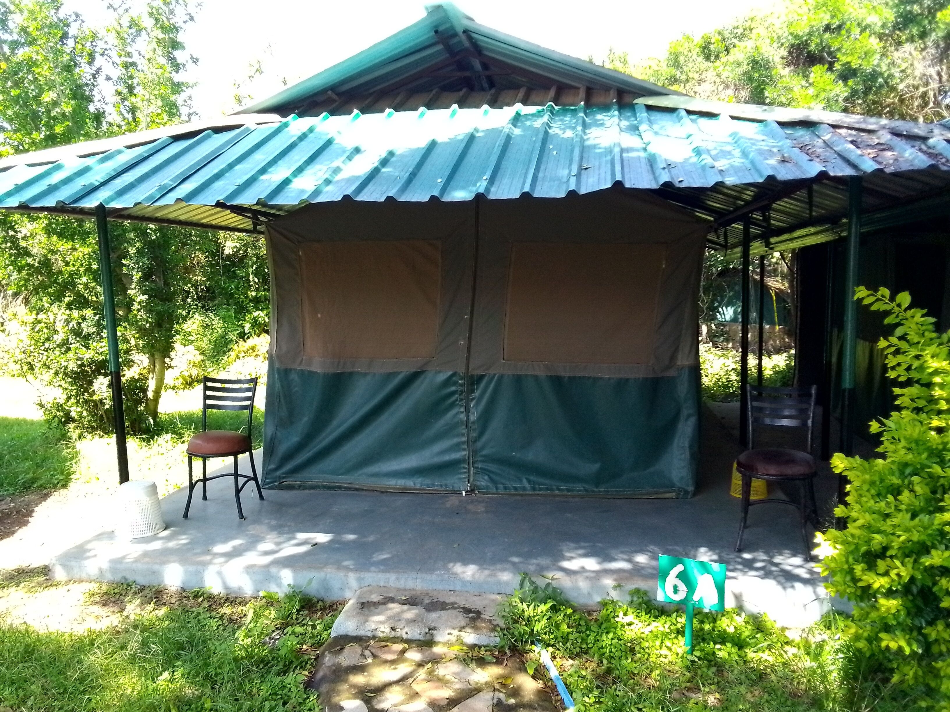 Un espacio de estar techado al aire libre con una mesa y sillas, rodeado de vegetación.