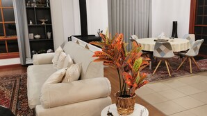 Un salon avec un canapé beige, une table à manger avec des chaises, une plante décorative et un réfrigérateur.