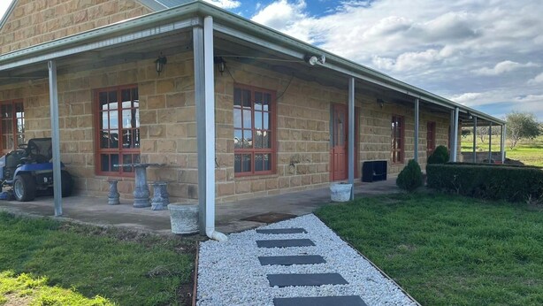 Un bâtiment en pierre doté d’un porche couvert, d’une pelouse et d’un chemin de gravier.