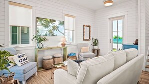 Un salon spacieux avec un canapé blanc, un fauteuil bleu et une grande fenêtre donnant sur des palmiers.