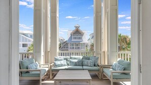 A covered outdoor seating area with a sofa and chairs, a table, and a view of a house in the background. - Premier Beach Home@Cinnamon Shore North w/ Private Pool, Fire Pit & More! (Port Aransas)