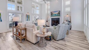 A spacious living room with a high ceiling, large windows, and a fireplace. - Premier Beach Home@Cinnamon Shore North w/ Private Pool, Fire Pit & More! (Port Aransas)