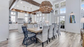 A spacious kitchen with white cabinets, a large island, and a dining area with wicker chairs. - Premier Beach Home@Cinnamon Shore North w/ Private Pool, Fire Pit & More! (Port Aransas)