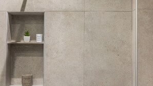 Ein Badezimmer mit einer beige gefliesten Wand, einem Regal mit einer Topfpflanze, einer Kerze und einem Schild mit der Aufschrift 'HARMONY'.