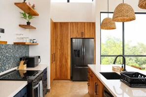 Une cuisine moderne avec des meubles en bois, un réfrigérateur noir et une grande fenêtre donnant sur un paysage verdoyant.