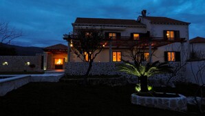 Una casa de dos pisos con fachada de piedra, una chimenea a la vista y una entrada bien iluminada.