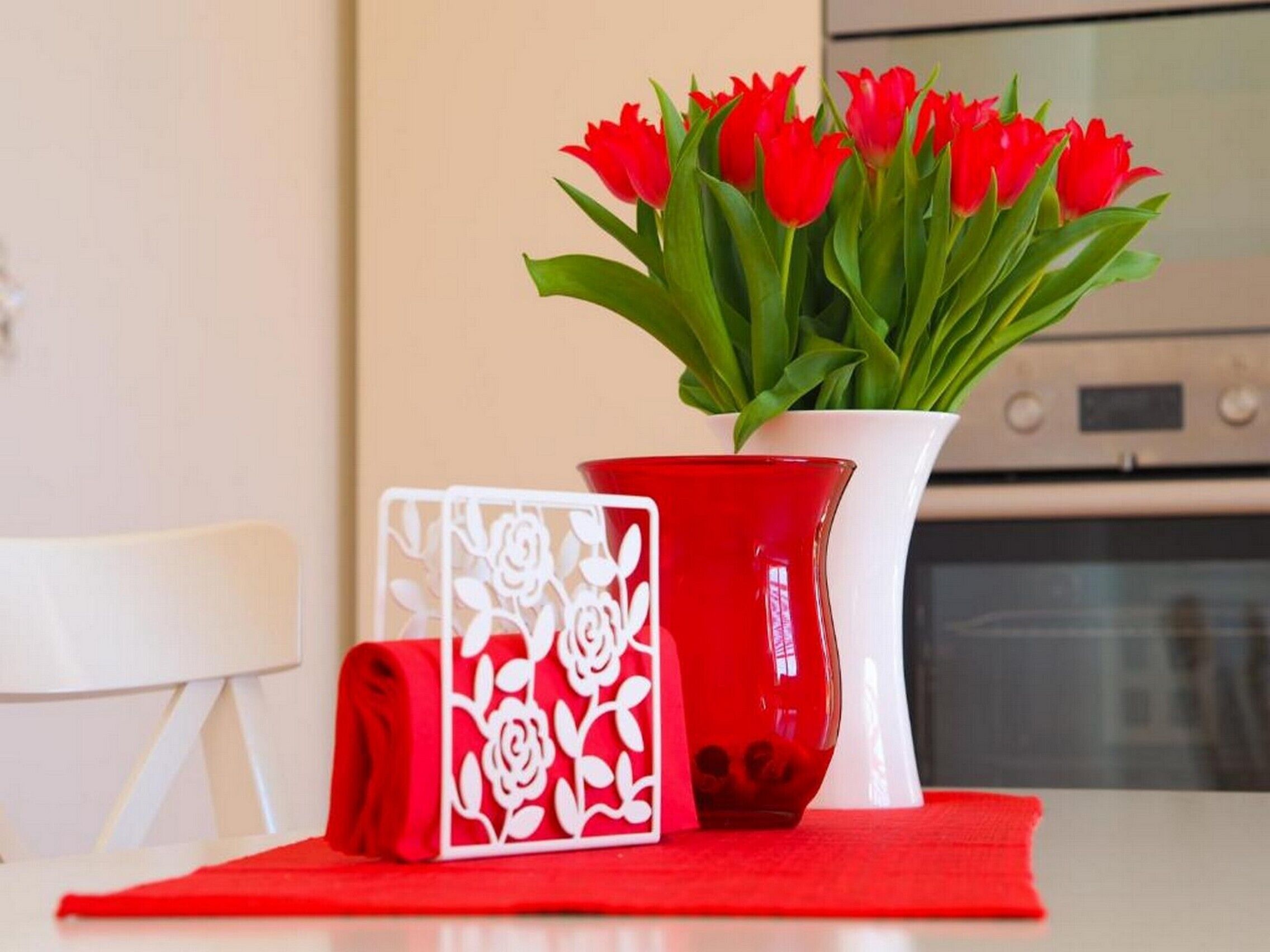 Ein Tisch mit einer roten Vase voller roter Tulpen, einem rot-weißen Dekorationsgegenstand und einem roten Tuch.