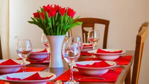 Una mesa de comedor dispuesta con servilletas rojas, platos blancos y copas de vino transparentes, junto con un florero de tulipanes rojos.