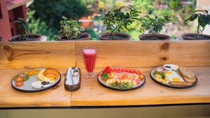 Una mesa de madera con cuatro platos de comida para el desayuno, un vaso de jugo rojo y plantas en macetas.