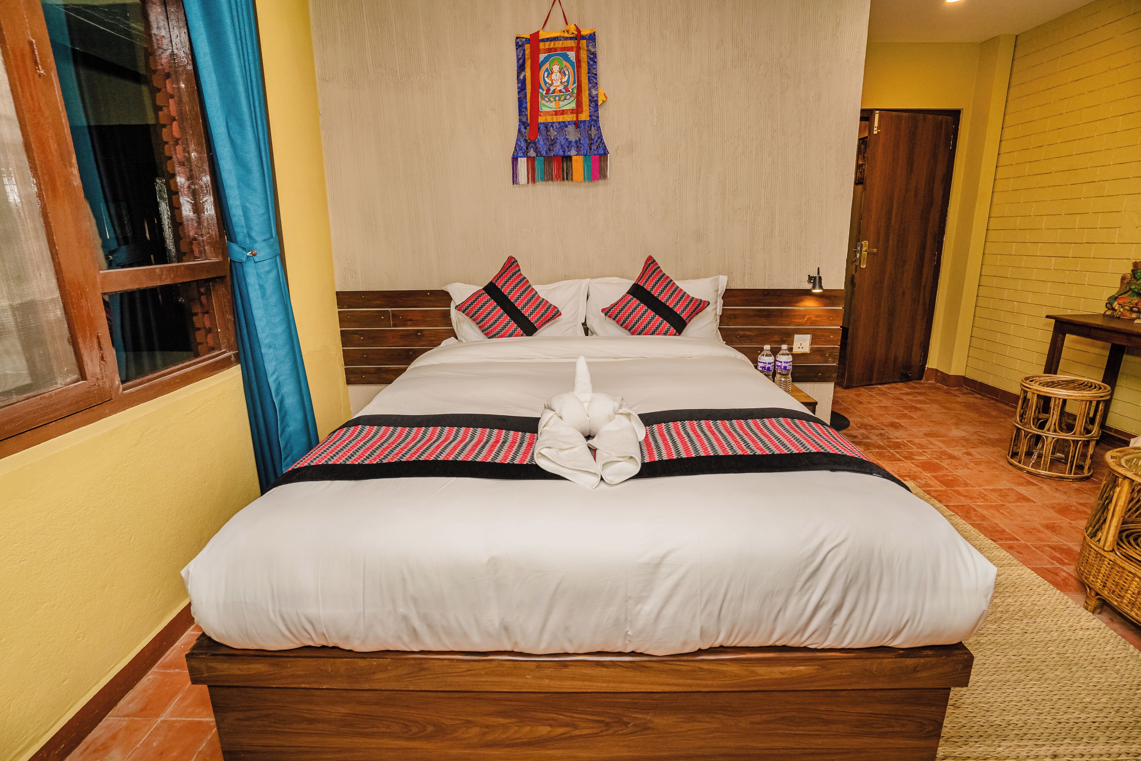 Una cama bien hecha con sábanas blancas y dos almohadas, un tapiz en la pared y una puerta de madera a la derecha.