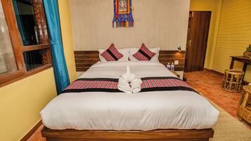 Una cama bien hecha con sábanas blancas y dos almohadas, un tapiz en la pared y una puerta de madera a la derecha.
