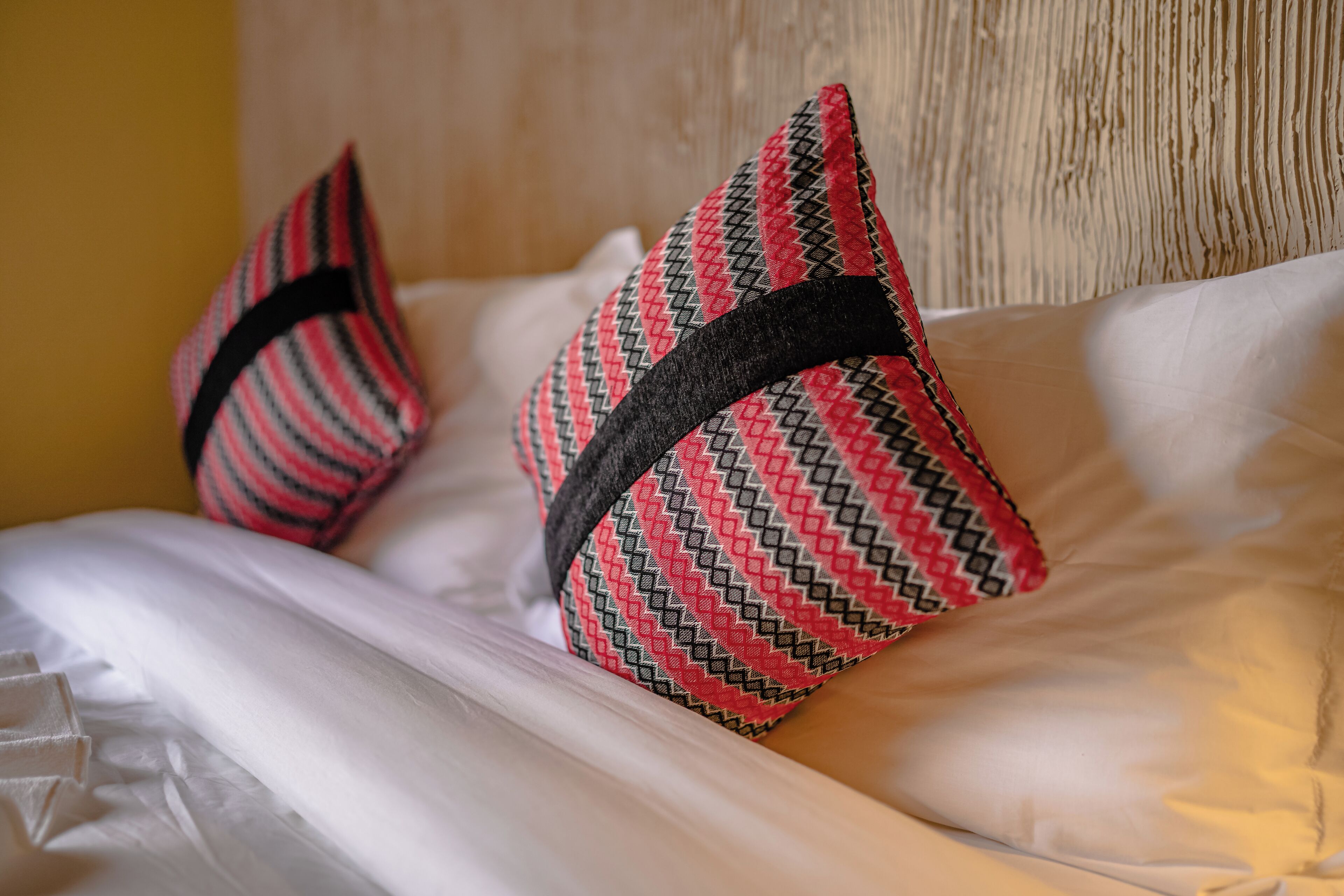 Una cama con sábanas blancas y dos almohadones decorativos de estampado geométrico.