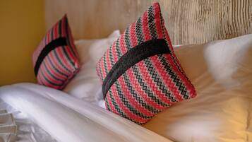 Una cama con sábanas blancas y dos almohadones decorativos de estampado geométrico.