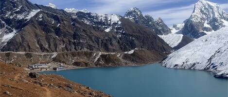 Un paisaje montañoso con un lago azul cristalino, terreno rocoso y un pequeño poblado con edificios cerca de la orilla.