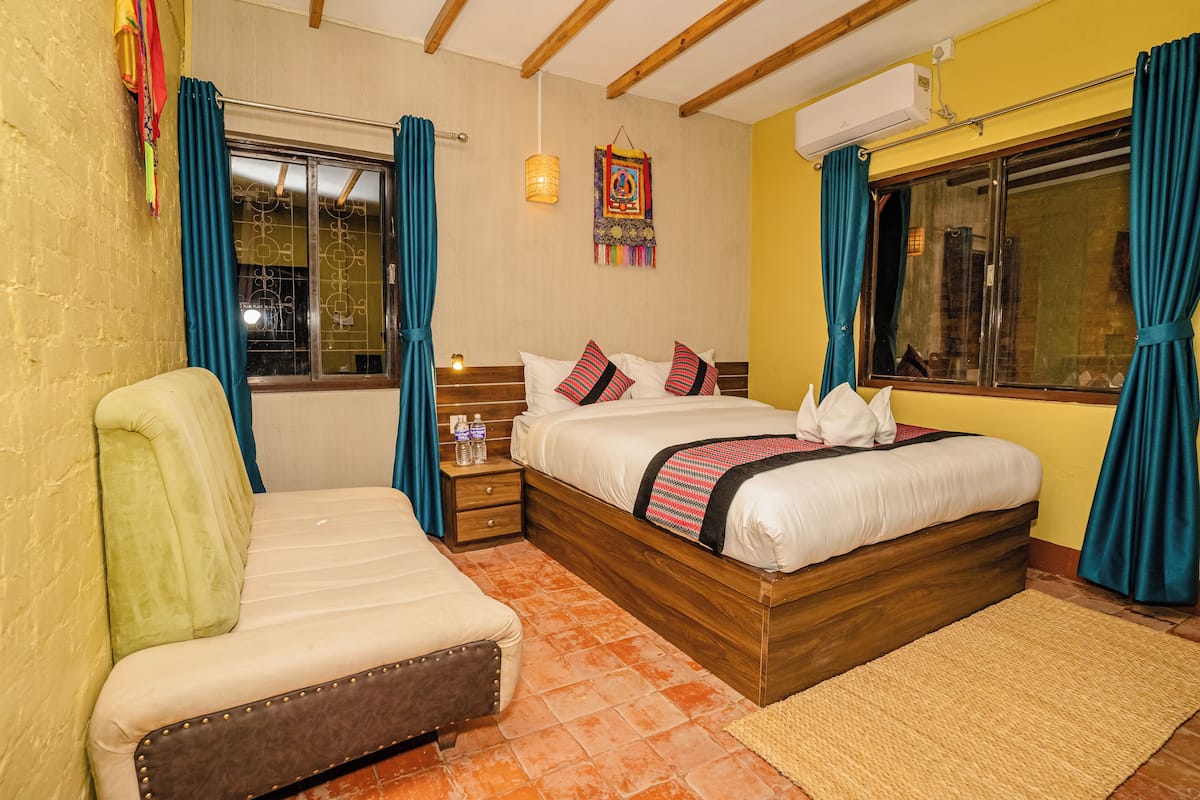 Un dormitorio con cama, sofá, mesita de noche y ventana con cortinas.