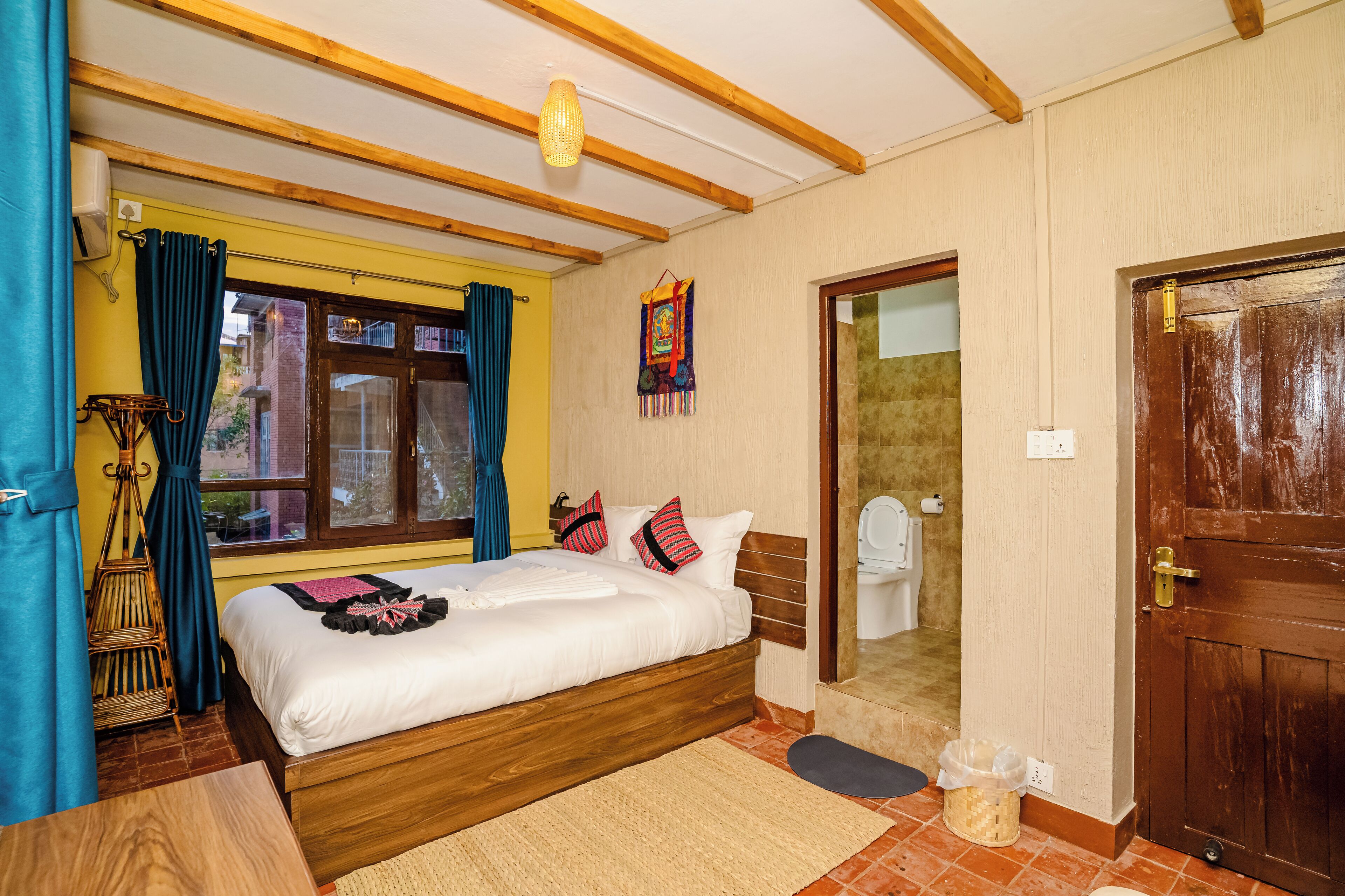 A bedroom with a wooden bed, a window with curtains, a small rug, and a wooden door.