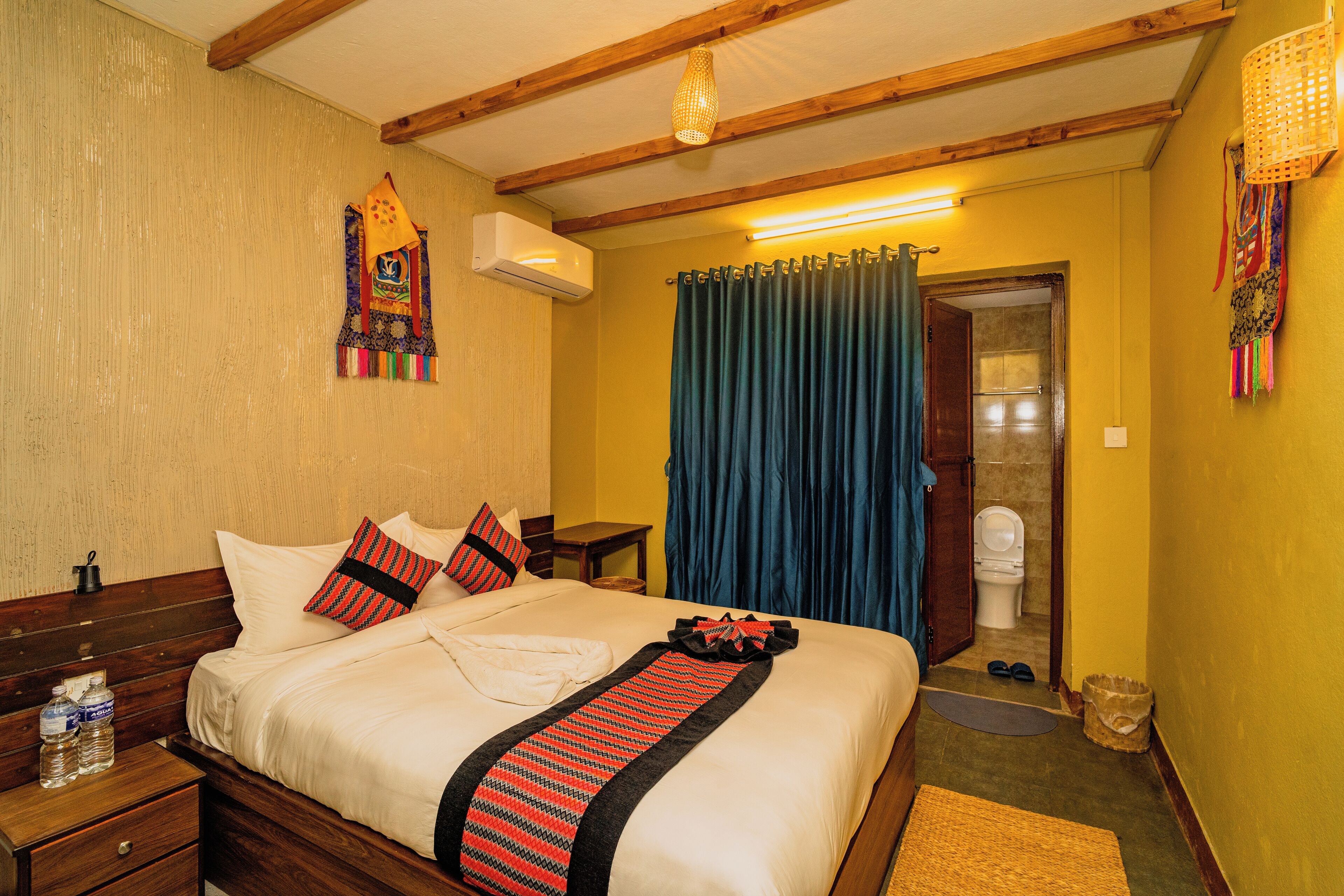 A hotel room with a wooden bed, a bedside table with a lamp, a bathroom with a toilet and shower, and a small hallway.