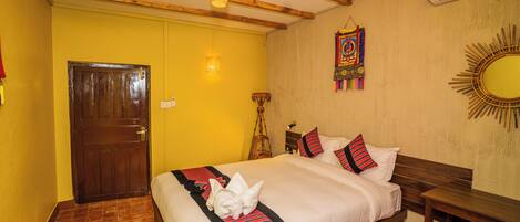 Habitación de hotel con cama de madera, una mesita pequeña, espejo fijado a la pared y un tapiz de colores.