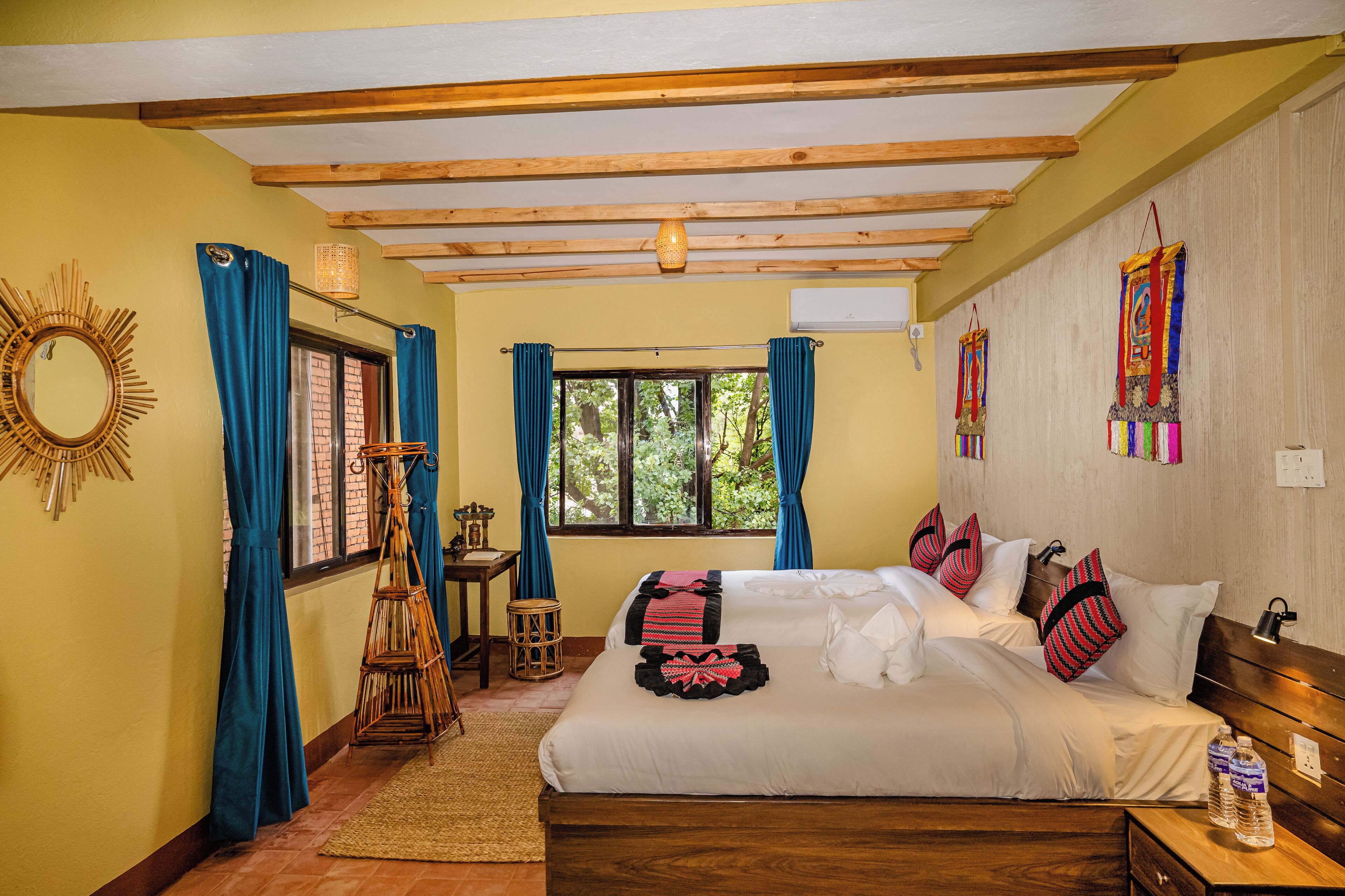 A well-lit bedroom with a wooden ceiling, a large bed with white linens, blue curtains, and a small table with a lamp.