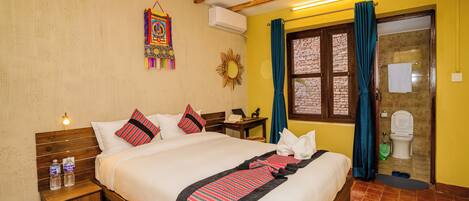 Habitación de hotel con cama de madera, mesita de noche con botellas de agua, decoración de sol y vistas al exterior a través de una ventana con cortinas.