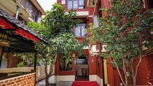 Un estrecho callejón con una alfombra roja que conduce a la entrada de un edificio, rodeado de árboles y un muro de ladrillo.