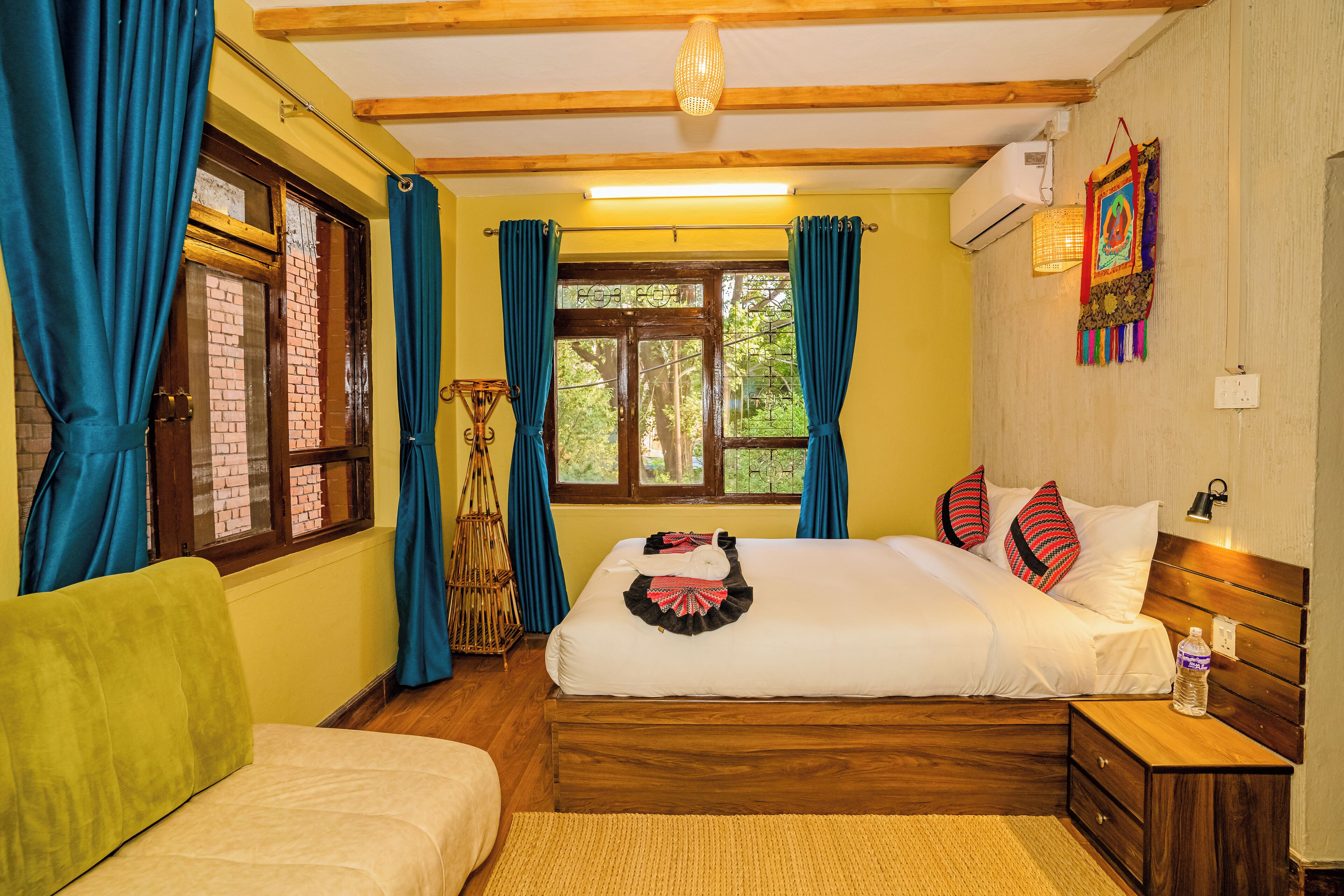 A room with two beds, a wooden headboard, a bedside table, a wall-mounted air conditioner, and a window with curtains.