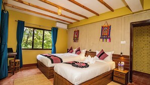 Una cama doble con sábanas blancas y almohadas rojas y negras, un cabecero de madera y una mesita de noche con dos botellas de agua.