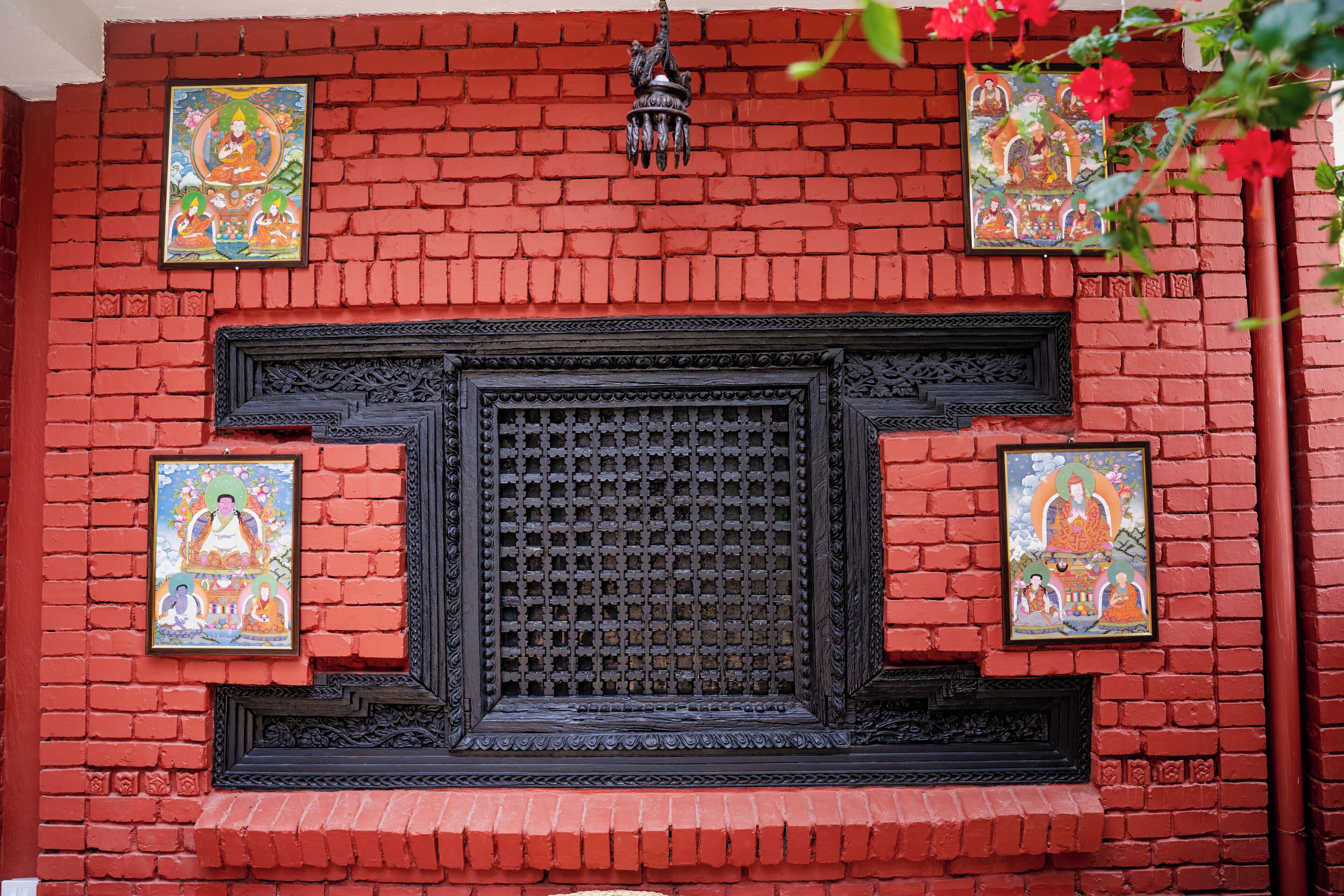 A red brick wall with a decorative window and two framed paintings.