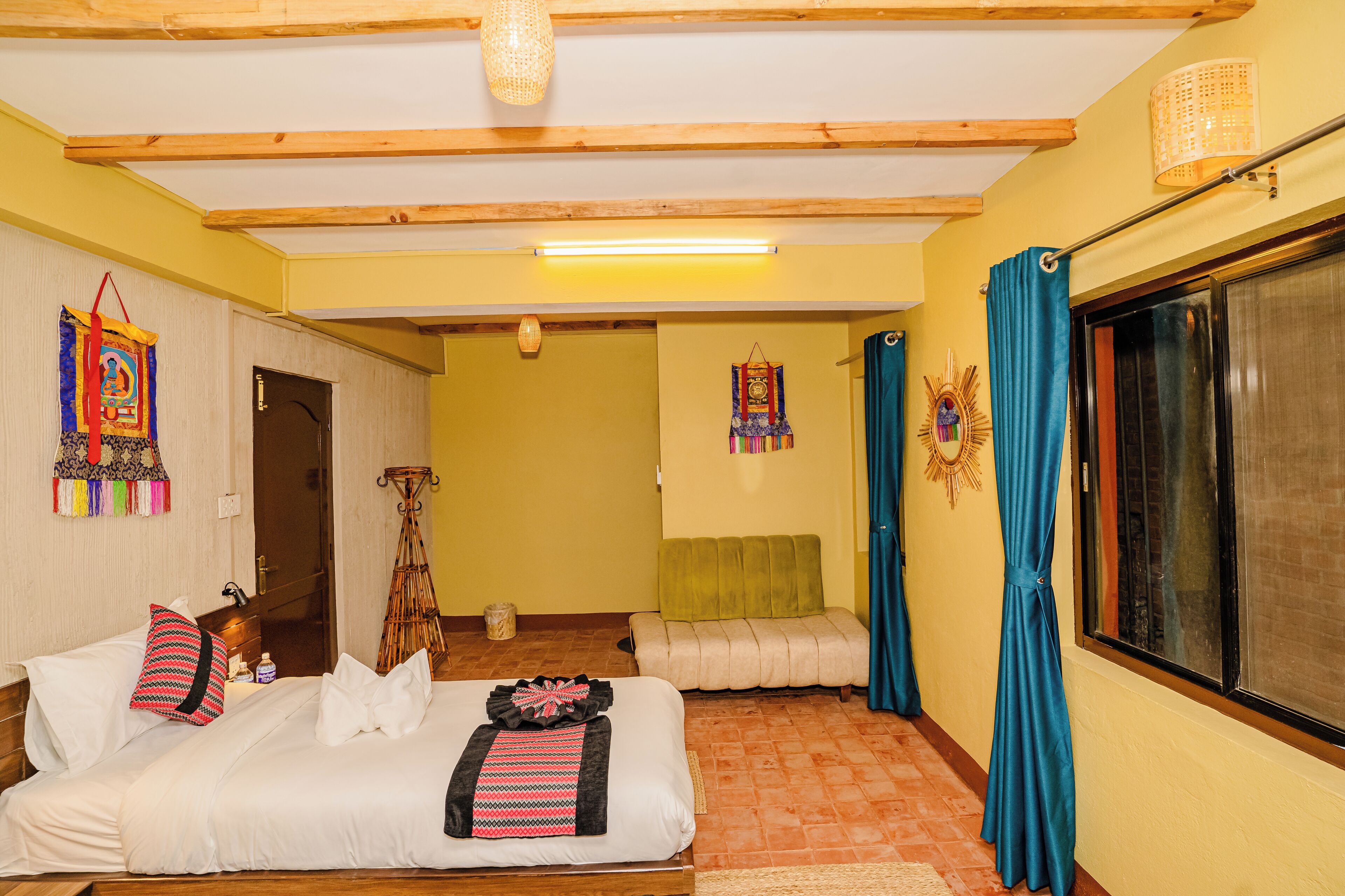 A hotel room with a bed, a sofa, a window with curtains, and a wall with decorative items.