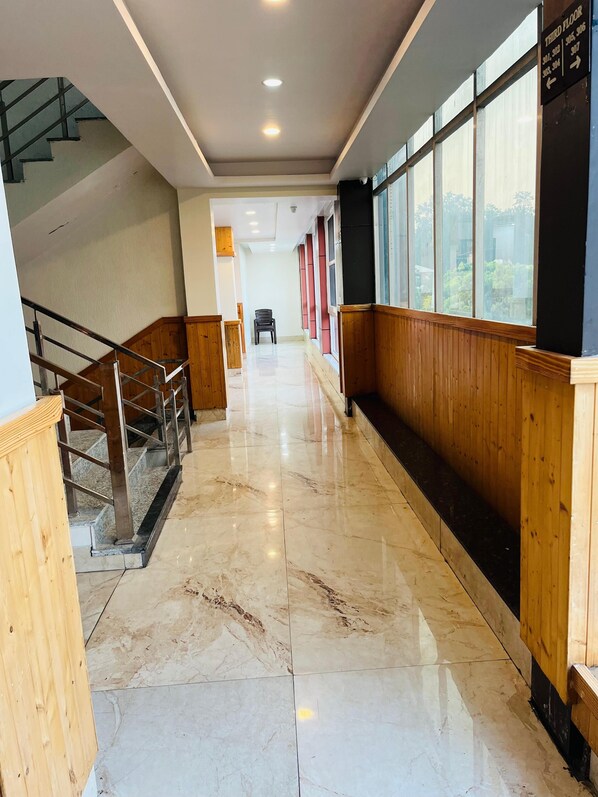 A corridor with a marble floor, wooden paneling, a staircase, and a view through large windows.