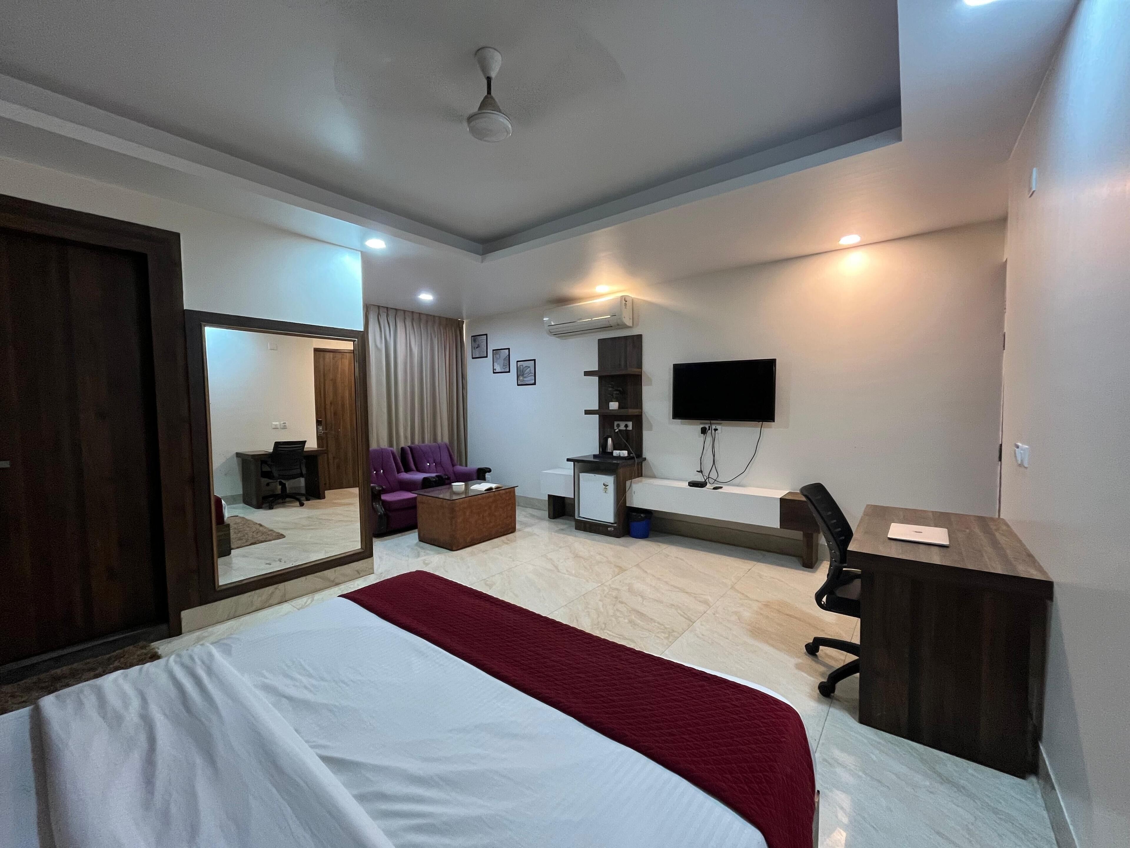 A hotel room with a large bed, a desk, a chair, a TV mounted on the wall, and a ceiling fan.