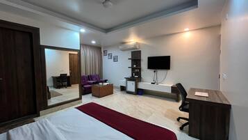 A hotel room with a large bed, a desk, a chair, a TV mounted on the wall, and a ceiling fan.