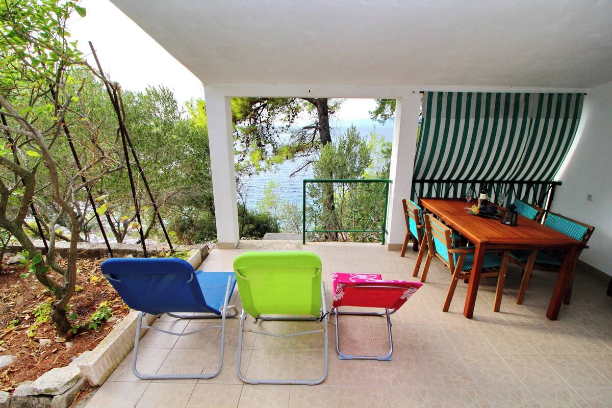 Un patio con mesa y sillas, vista a árboles y agua, y una cortina verde a rayas.