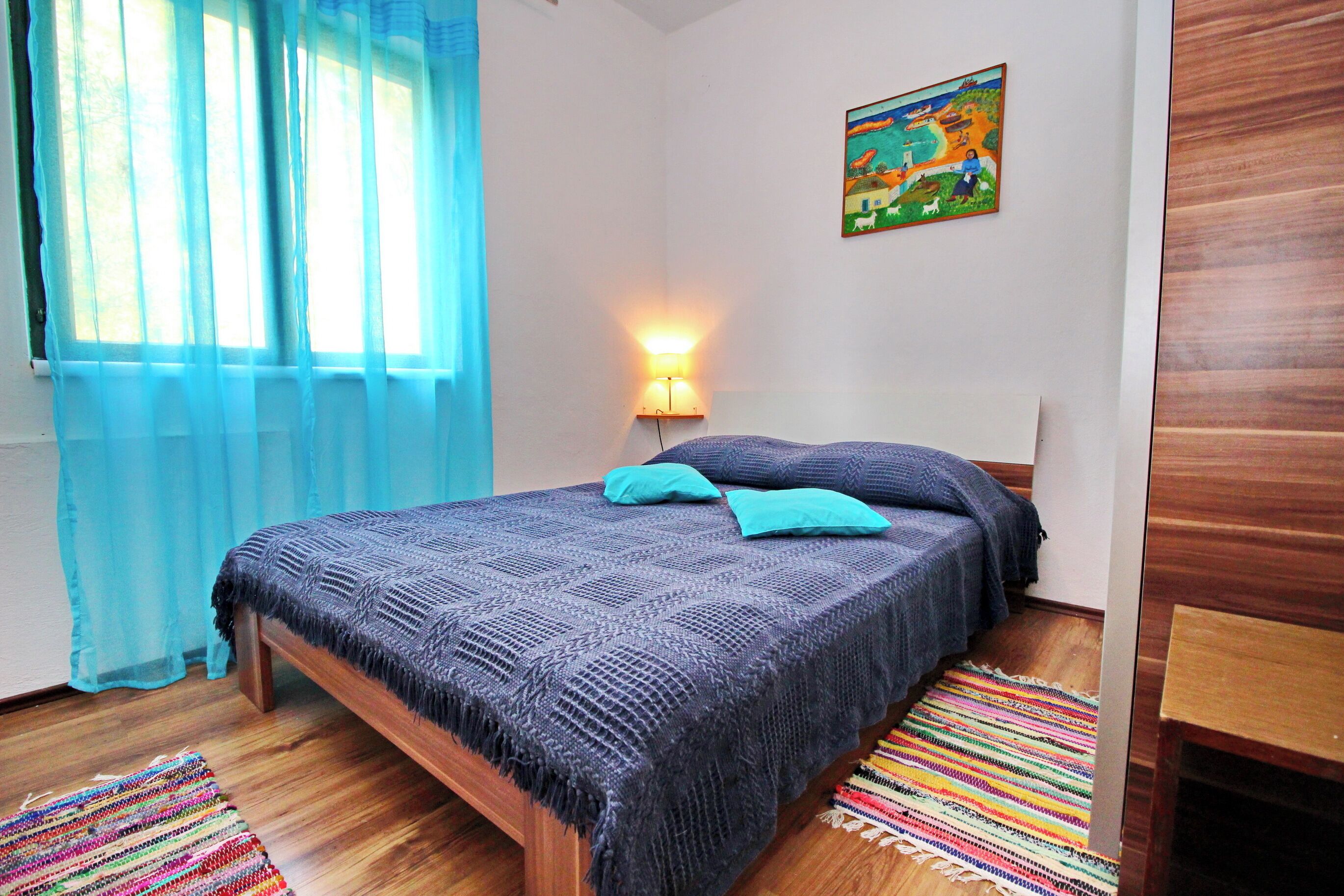 Un dormitorio con cama, una mesita de noche con lámpara, una alfombra colorida y un cuadro en la pared.