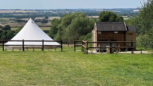 A tent and a wooden building in a grassy field with a view of distant fields and trees. - Luxury Bell Tents with beautiful views (Lower Boddington)