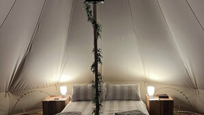 A tented accommodation with a bed, bedside tables, and a hanging plant. - Luxury Bell Tents with beautiful views (Lower Boddington)