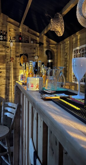 A rustic wooden bar area with various bottles and glasses, a clock, and a hanging light fixture. - Luxury Yurt with beautiful views (Lower Boddington)