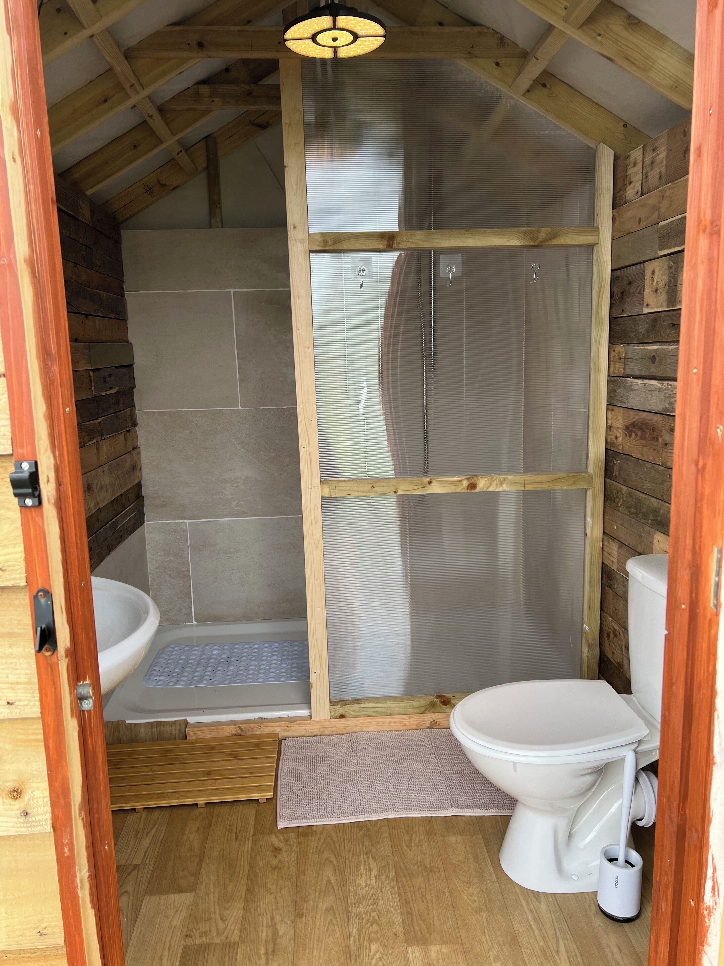 Et lille badeværelse i en træhytte med bruser, toilet og håndvask.