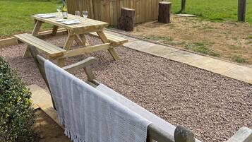 A picnic setup with a wooden table and benches, surrounded by a gravel path and a grassy field.