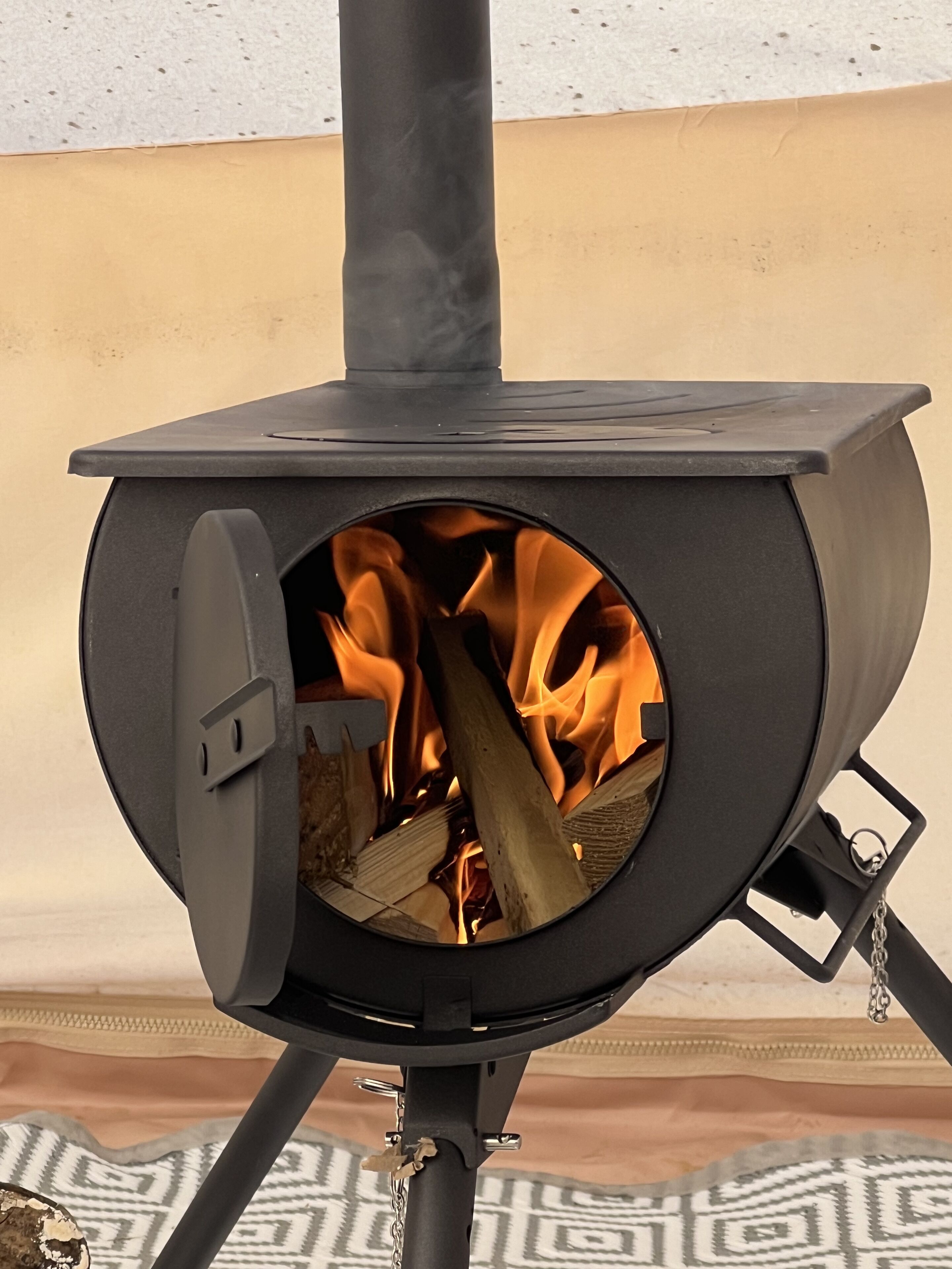 Un poêle à bois doté d’une ouverture circulaire, contenant des bûches et muni d’une grille métallique.