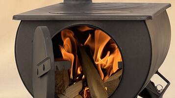 Un poêle à bois doté d’une ouverture circulaire, contenant des bûches et muni d’une grille métallique.