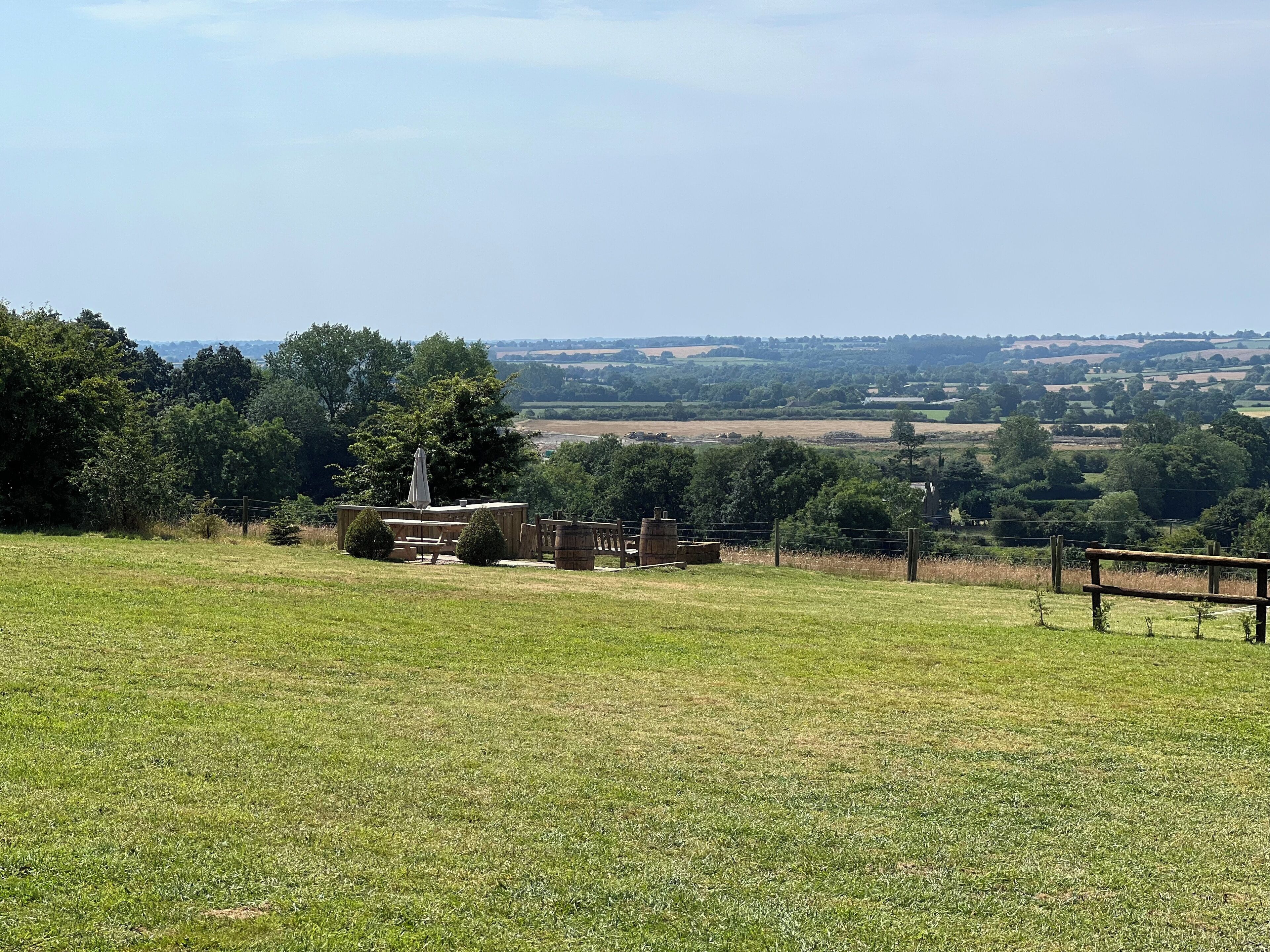 A grassy field with a wooden structure, possibly a picnic area, and hay bales.