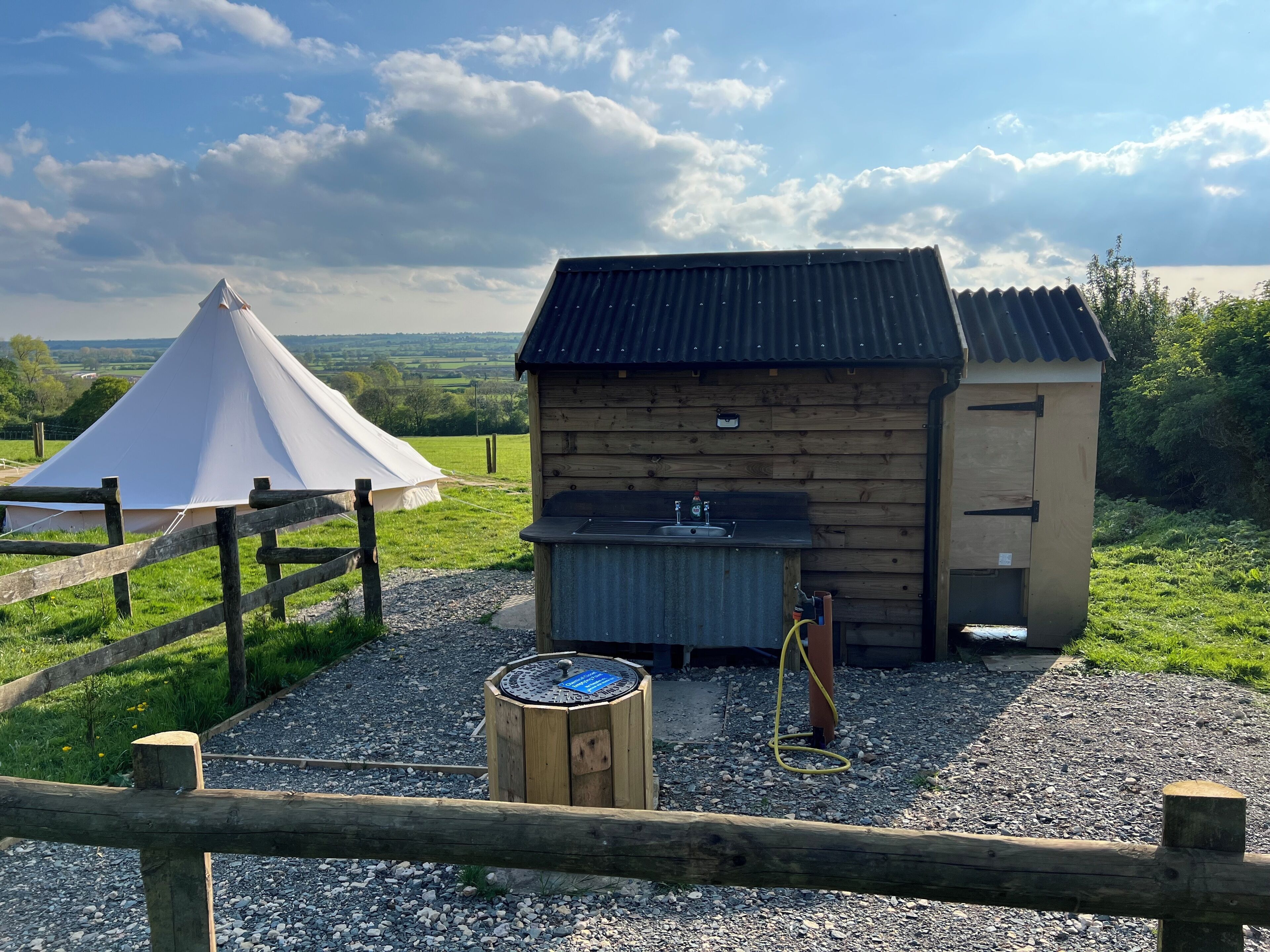Een rustieke houten cabin met een metalen dak, een klein spoelbakje en een waterslang.
