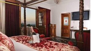 A four-poster bed with rose petals, a wooden desk, a large window, and a chandelier.