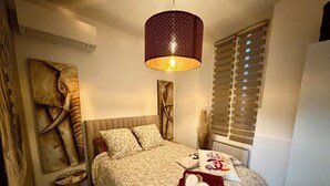 Un dormitorio con cama, lámpara colgante, ventana con persianas y radiador fijado a la pared.