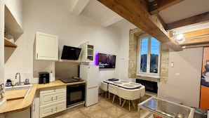 Cocina compacta con encimera de madera, armarios blancos, horno empotrado y comedor con mesa y sillas de vidrio.